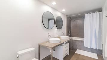 Een moderne badkamer met toilet, twee wastafels, een douche en een bad.