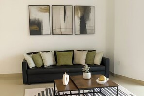 A modern living room with a black sofa, green and white cushions, a coffee table with a white vase and a bowl, and three abstract paintings on the wall. - Brickell Avenue - City Centre Suites (Miami)