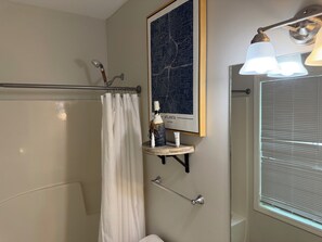 Un baño con cortina de ducha, un mapa enmarcado de Atlanta, un estante con artículos de aseo y una ventana con persianas.