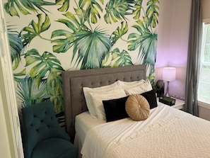 A bedroom with a bed, a nightstand, a lamp, and a chair.