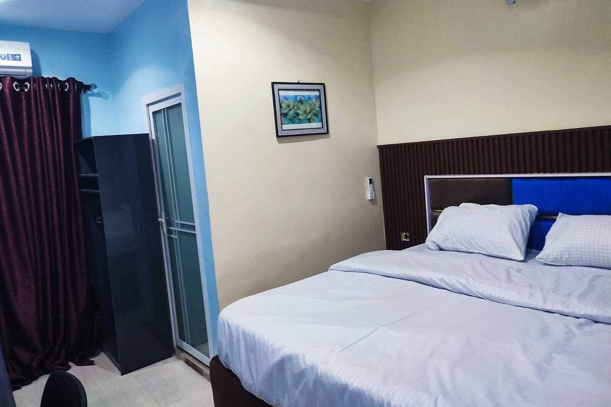Habitación de hotel con cama, ventana con cortinas, un cuadro en la pared y un ventilador de techo.