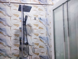Une douche dotée d’un pommeau de douche à effet pluie et d’un pommeau de douche à main, d’une porte en verre et d’un mur à motifs de marbre.