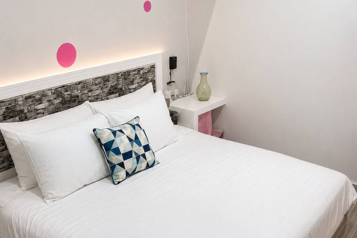 A neatly made bed with white linens, a patterned pillow, and a stone-textured headboard.