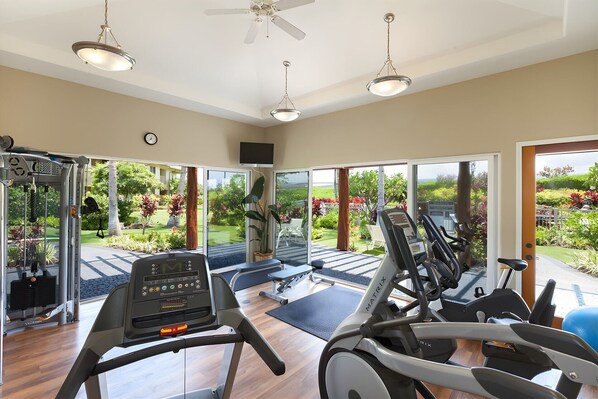 A gym with treadmills, a weight machine, and a large window overlooking a garden.