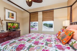 A bedroom with a bed, a TV, a dresser, and a window with a view.