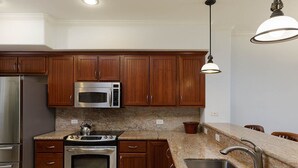 A modern kitchen with wooden cabinets, stainless steel appliances, granite countertops, and a pendant light.