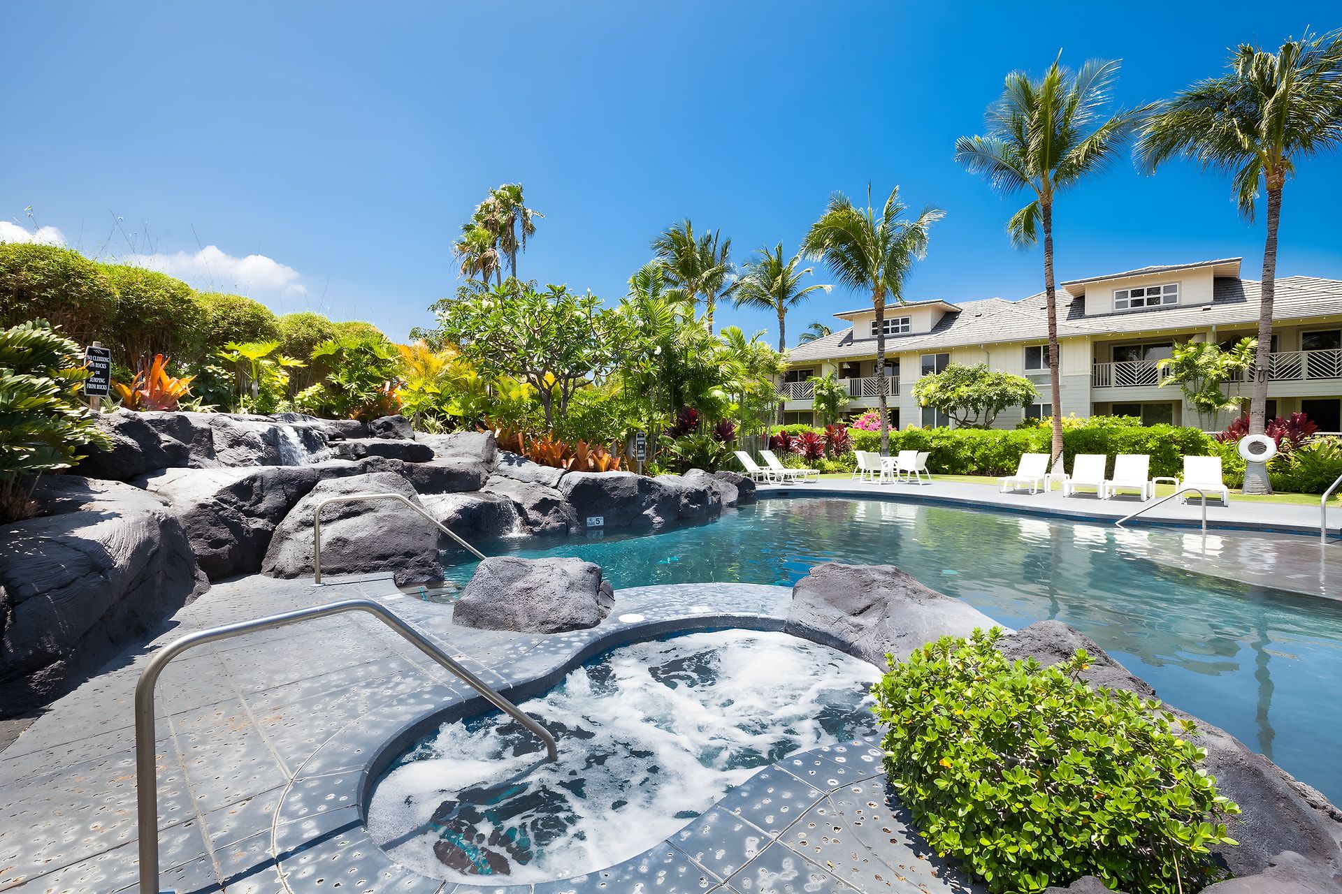 A hotel pool area with a hot tub, lounge chairs, and a waterfall feature.