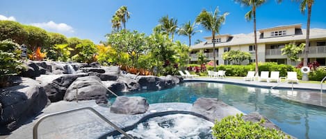 A hotel pool area with a hot tub, lounge chairs, and a waterfall feature.