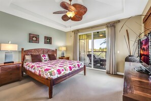 Een slaapkamer met een bed, nachtkastjes, een plafondventilator, een balkon met uitzicht en een schilderij aan de muur.