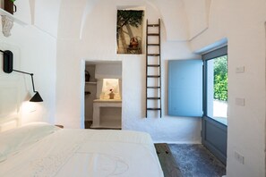 A bedroom with a bed, a ladder, a small shelf with a plant, and a window. - Masseria Ramunno Piccola - Anna Suite by Rentbeat (Ostuni)