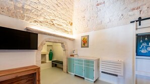 Ein Zimmer mit einer Steinwand, einer Holzbank, einem türkisblauen Schrank, einem weißen Heizkörper und einem an der Wand montierten Flachbildfernseher.