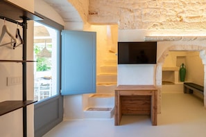 A room with a stone wall, a wooden bench, a white door, and a view of the outside. - Masseria Ramunno Piccola - Anna Suite by Rentbeat (Ostuni)
