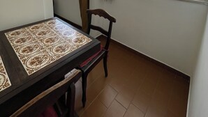 A room with a tiled table, a chair, a window with curtains, and a view of buildings outside. - Sugarloaf - Rio Sul 2 bedroom apartment (Rio de Janeiro)
