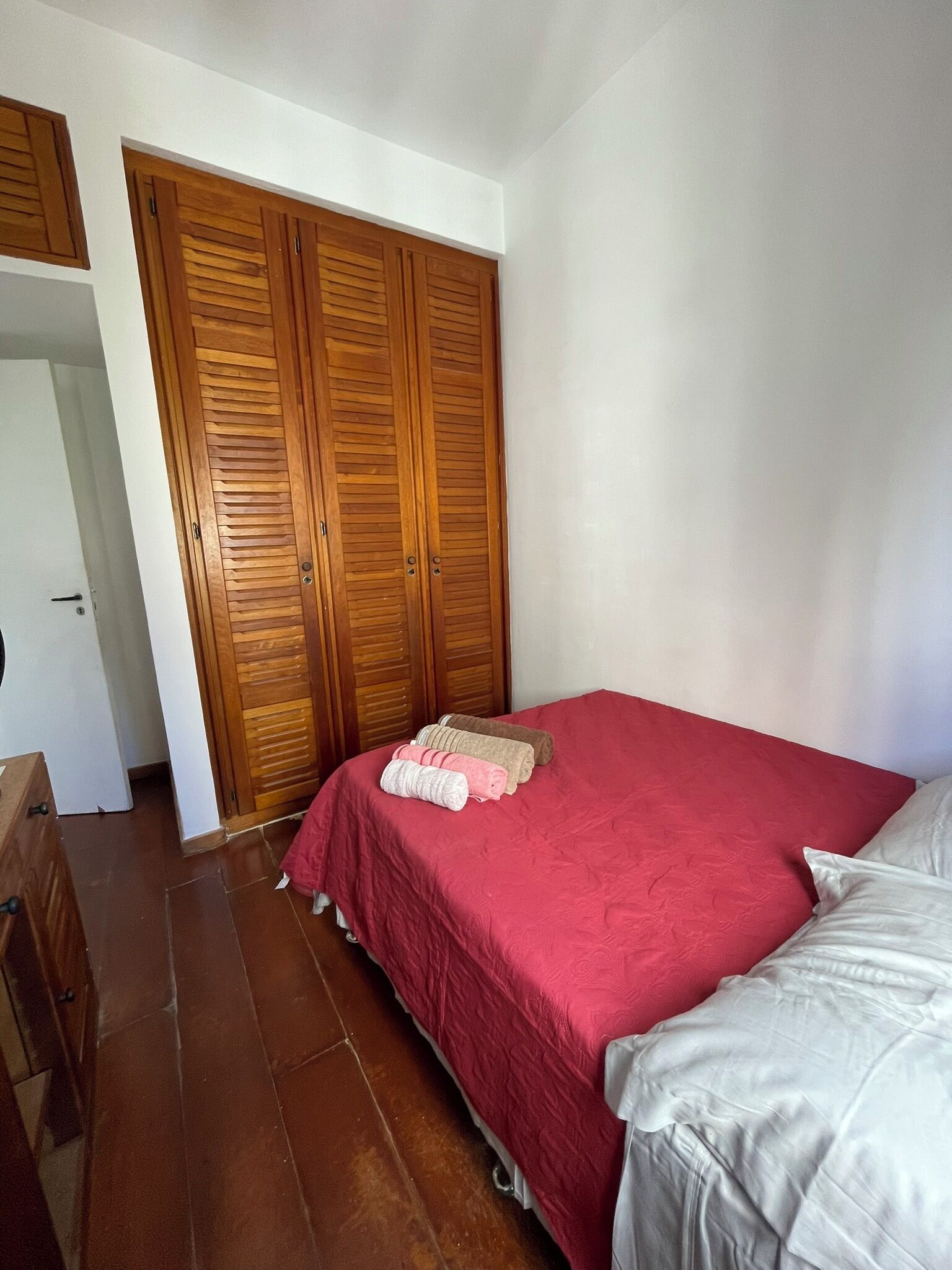 A bedroom with a bed, a wooden wardrobe, and a tiled floor.