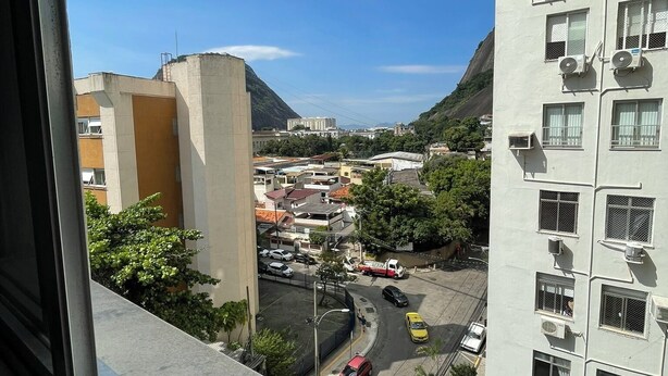 A high-rise building with multiple air conditioning units, a parking lot with various vehicles, and a mountainous landscape in the background. - Sugarloaf - Rio Sul 2 bedroom apartment (Rio de Janeiro)