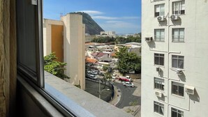 A high-rise building with multiple air conditioning units, a view of a cityscape with buildings and a mountain, and a clear sky. - Sugarloaf - Rio Sul 2 bedroom apartment (Rio de Janeiro)