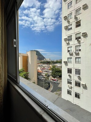 Ein Hochhaus mit mehreren Klimaanlagen, Blick auf eine Stadtlandschaft mit Gebäuden und einem Berg, und ein klarer Himmel.