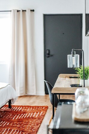 Una habitación moderna con cama, escritorio, silla, planta en maceta y una puerta.