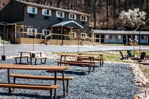 A building with multiple windows and a covered entrance, surrounded by gravel and wooden picnic tables.