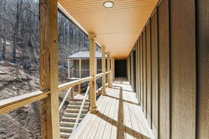 A wooden deck with railings, a staircase, and a view of a forested area.