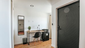 A compact room with a wooden floor, a desk with a chair, a small black refrigerator, a microwave, a potted plant, a mirror, and a black door. - King Deluxe Suite on Afton Mtn | Pet-Friendly! (Waynesboro)