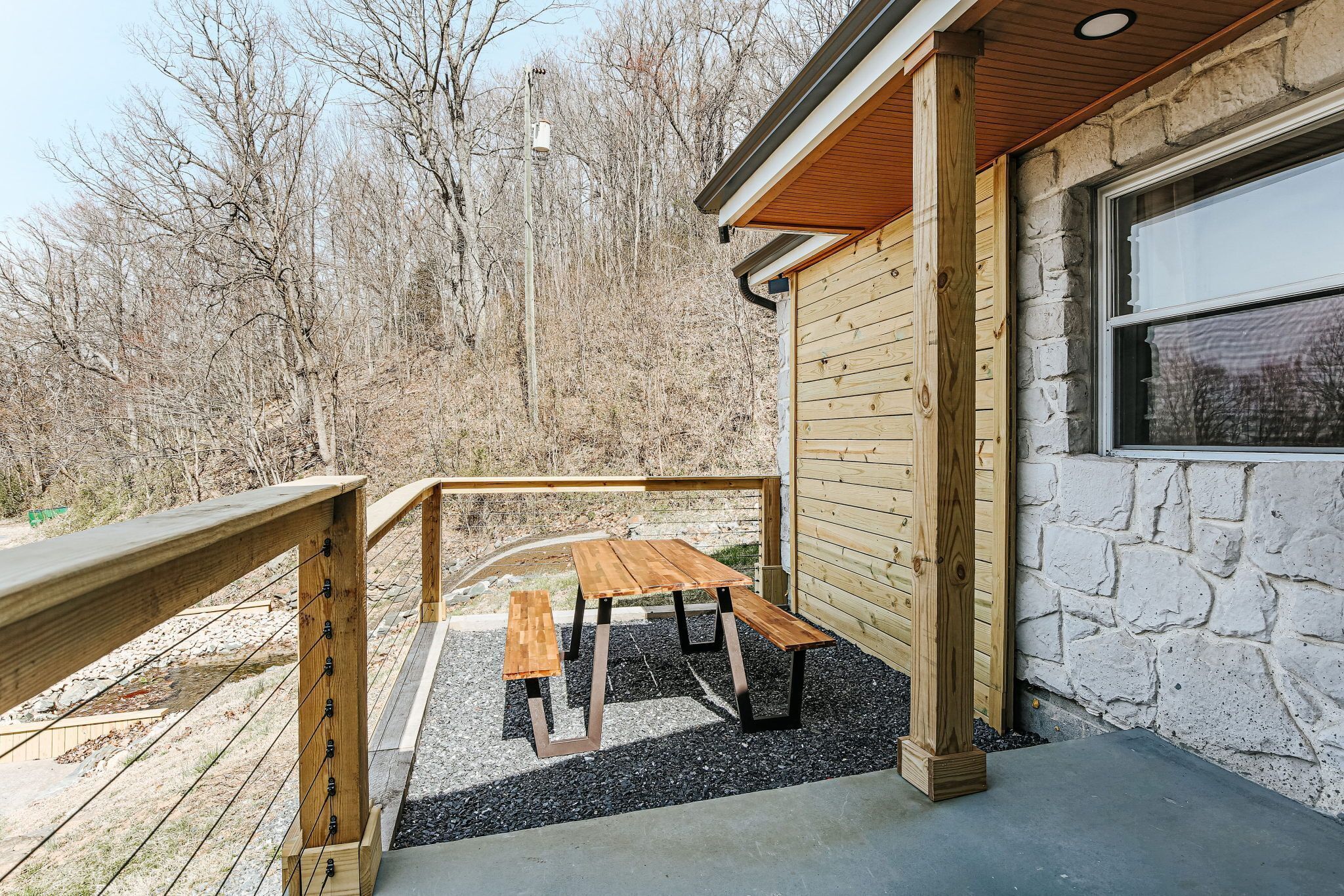 A wooden deck with a picnic table and benches, a stone wall, and a wooden railing.