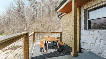 A wooden deck with a picnic table and benches, a stone wall, and a wooden railing.
