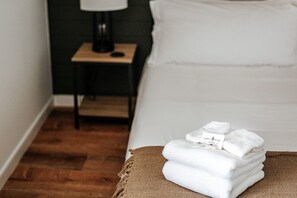 Una cama bien hecha con sábanas blancas y una pila de toallas dobladas sobre un cojín marrón.
