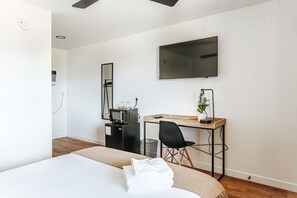 A hotel room with a bed, a desk with a computer, a TV, and a mirror.