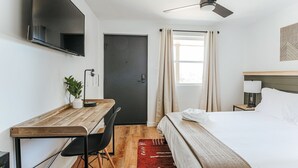 Habitació d'hotel amb llit, escriptori, cadira, televisió i finestra amb cortines.