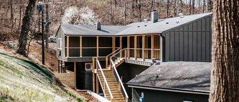 A two-story building with a staircase leading to a deck, surrounded by trees.