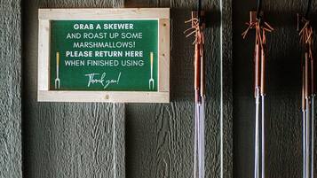 A sign with a skewer and marshmallows, and three skewers on a wooden surface.