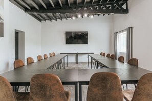 Uma sala de conferências com uma mesa comprida e cadeiras, um quadro na parede e uma janela com cortinas.