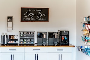 A coffee bar with multiple espresso machines, a Keurig display, and a sign that reads 'Complimentary Coffee Bar Please Help Yourself!'