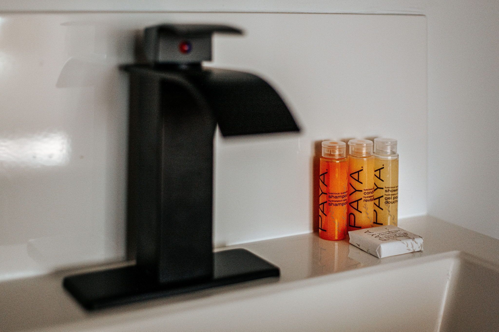 Een badkamer met een zwarte kraan, drie flessen shampoo en een zeepstuk op een wit aanrecht.