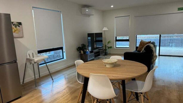 A modern room with a round wooden table, white chairs, a sofa, a TV, and a window with a view. - 3BR Haven in Stony Rise (Stony Rise)