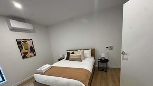 A bedroom with a bed, bedside table, and a wall-mounted air conditioner. - 3BR Haven in Stony Rise (Stony Rise)