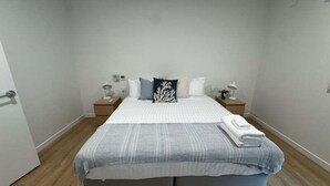 A bedroom with a bed, two bedside tables, a nightstand, a wall-mounted light, and a door. - 3BR Haven in Stony Rise (Stony Rise)