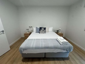 A bedroom with a bed, two bedside tables, a nightstand, a wall-mounted light, and a door. - 3BR Haven in Stony Rise (Stony Rise)