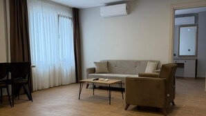 A spacious living area with a sofa, a coffee table, and a chair. There is an air conditioning unit on the wall and a door leading to another room. - Mimoza Apart (TRABZON)