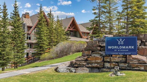 A stone wall with a sign for Canmore-Banff Resort, surrounded by trees and a building with a sloped roof. - Serene location, spaceous with pool and easy access to Banff and Lake Louise (Canmore)