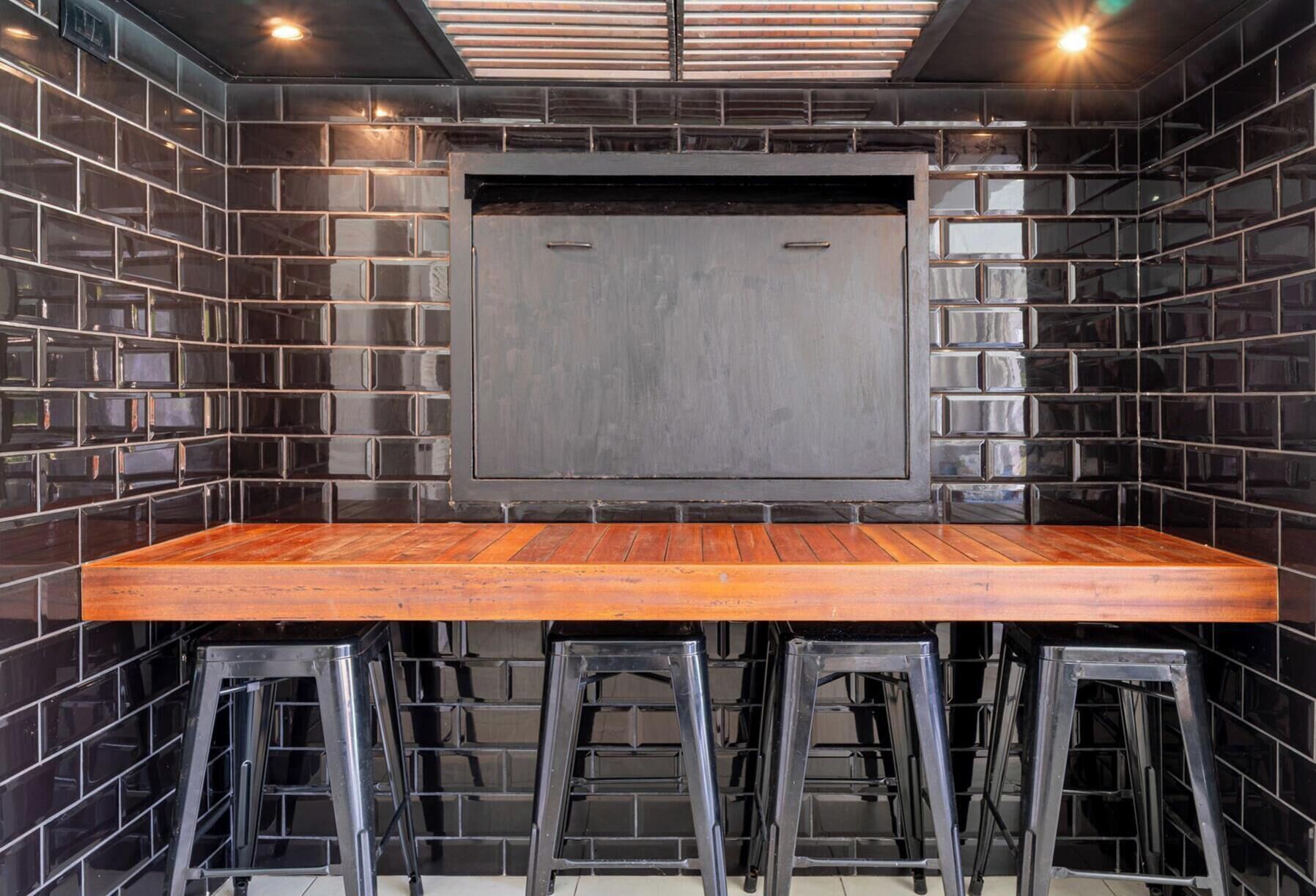 Une pièce avec une longue table en bois, des chaises en métal noir et un mur recouvert de carreaux noirs.