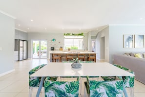A modern kitchen with a central island, a dining area with a white table and chairs, and a grey sofa in a bright living space.
