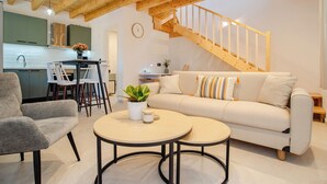 A modern living room with a wooden staircase, a sofa, two round tables, and a dining area with chairs. - 25 meters from the beach (Lefkimmi)