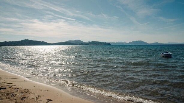 A beach with calm water, a boat, and distant mountains. - 25 meters from the beach (Lefkimmi)