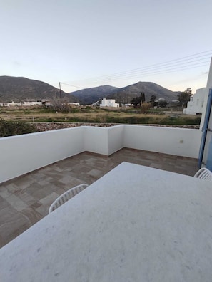 Eine Terrasse mit weißem Tisch und Stühlen, umgeben von weißen Mauern, mit Blick auf entfernte Gebäude und Berge.