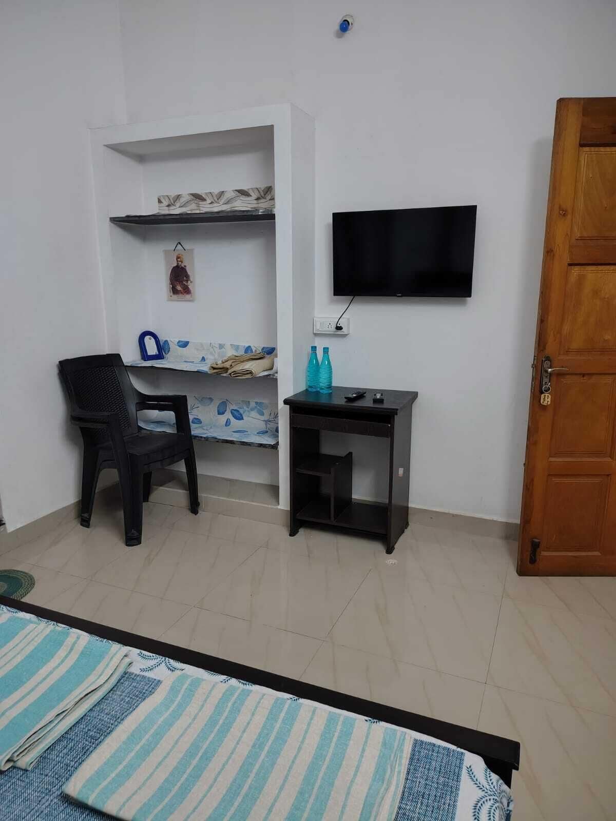 Una habitación con cama, escritorio, silla, televisor y puerta.