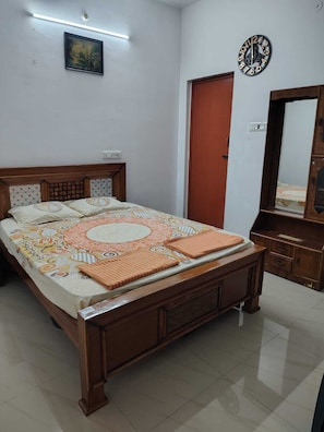 Quarto com cama de madeira, mesa de cabeceira, espelho, relógio e um quadro na parede.