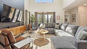 Amplia sala de estar con una televisión de pantalla plana grande, un sofá modular, una mesa de centro y una chimenea.