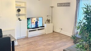 A modern living room with a television, a chandelier, a dining table, and a potted plant. - 
Cossy two bedroom apartment in Canning Town (London)